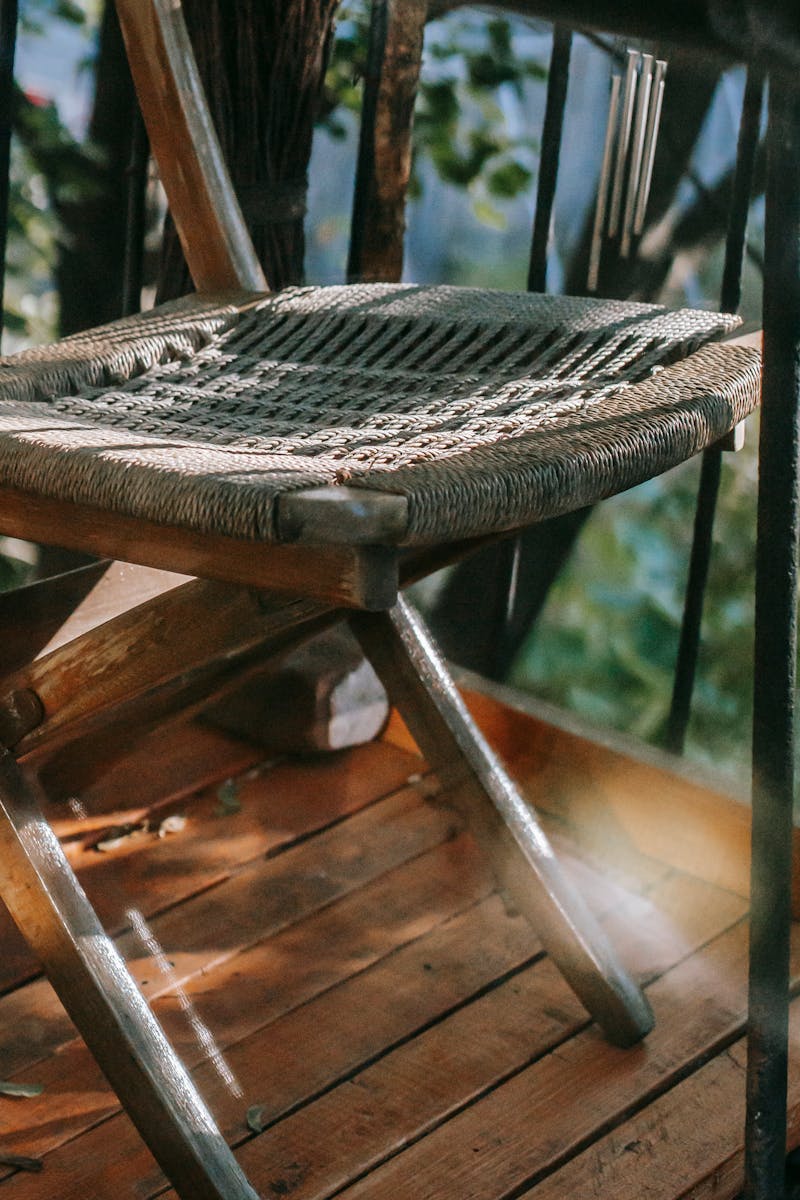 Comfortable shabby wooden chair with wicker seat placed on wooden floor of balcony on summer sunny day